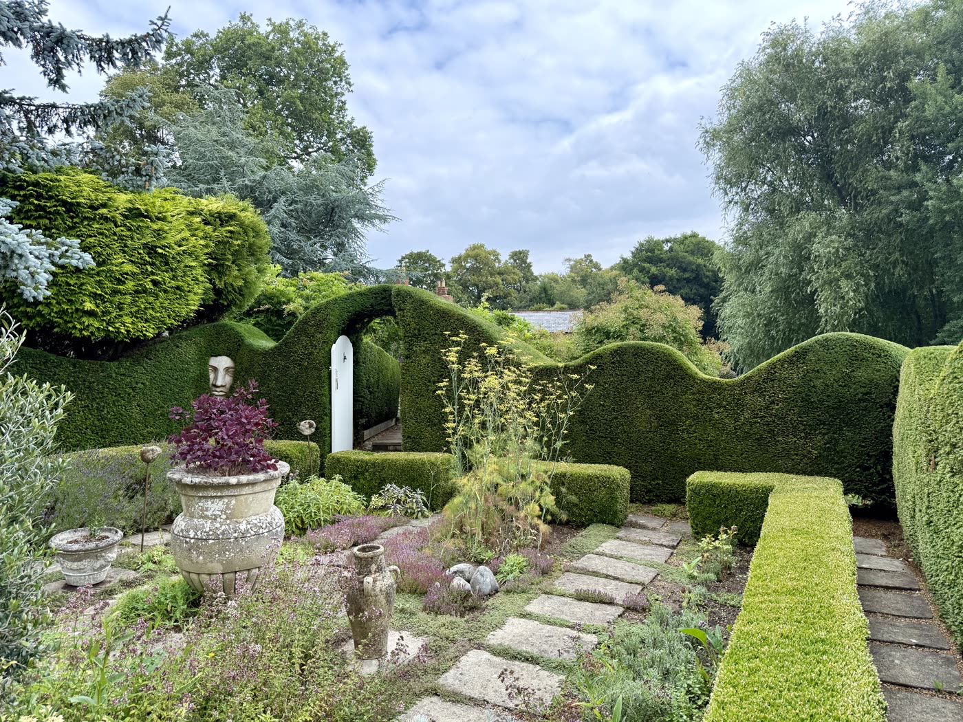 Sculpted yew hedge garden with a stone-face statue and a topiary door archway